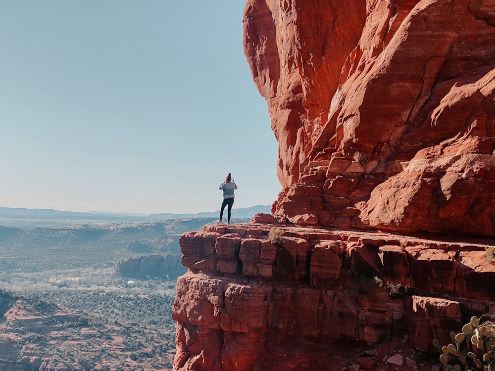 man standing on brown rock formation near body of water during daytime