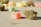 Colorful gummy candies and dried herbal buds are scattered on a flat surface. The focus is on a bright red gummy candy and a cannabis bud in the foreground, with other candies and buds slightly blurred in the background.