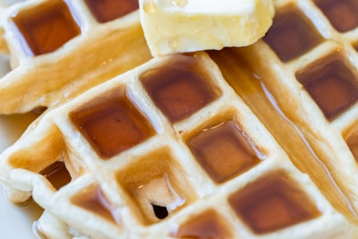 Close-up of a crispy fried chicken piece resting on a golden waffle drizzled with maple syrup.