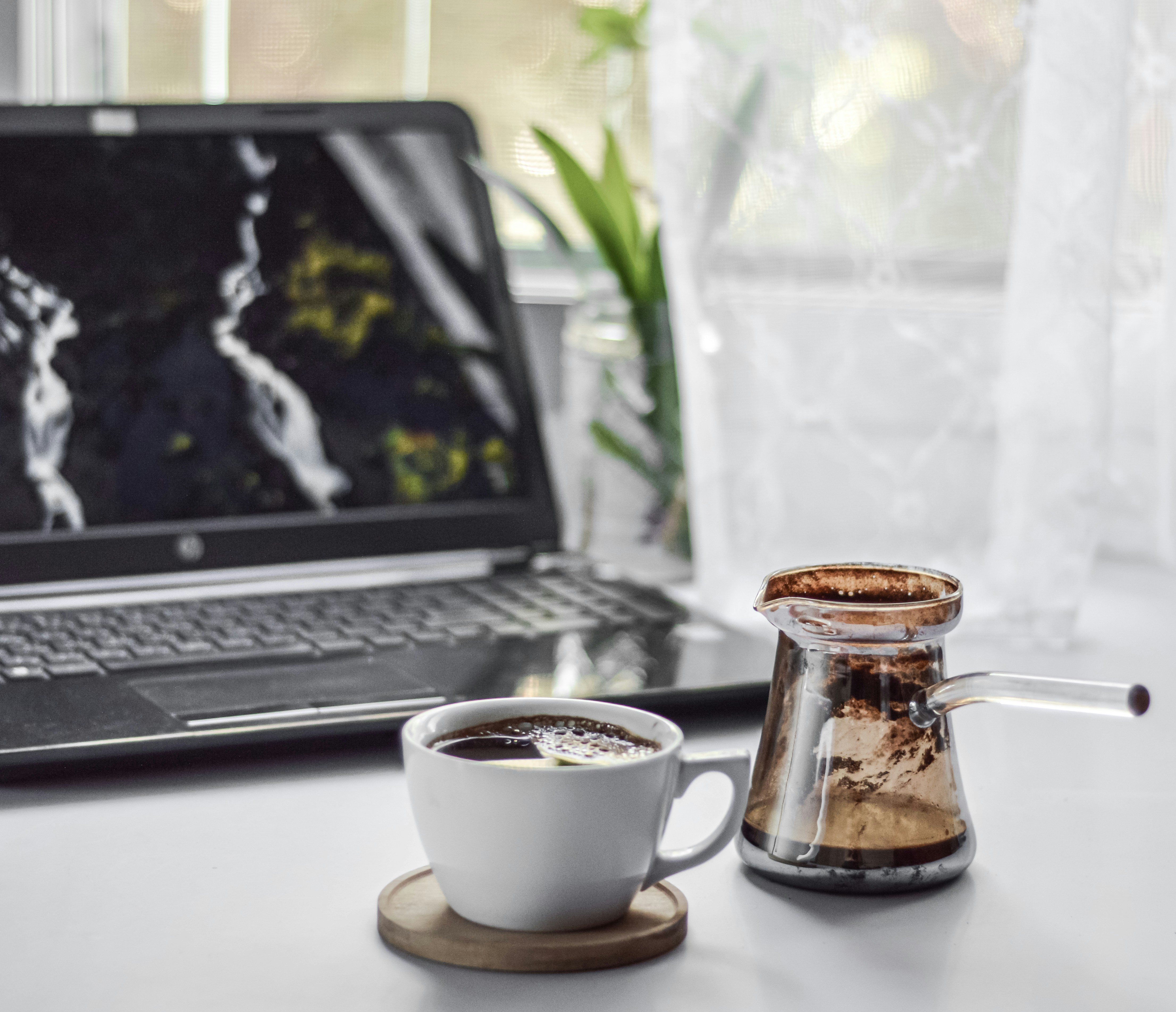 Laptop beside a coffee pot and white cup