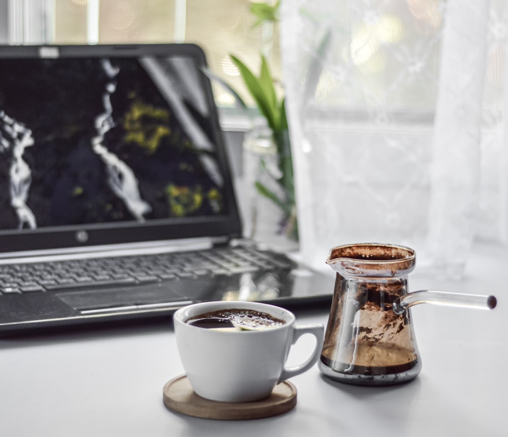 macbook pro beside white ceramic mug on table