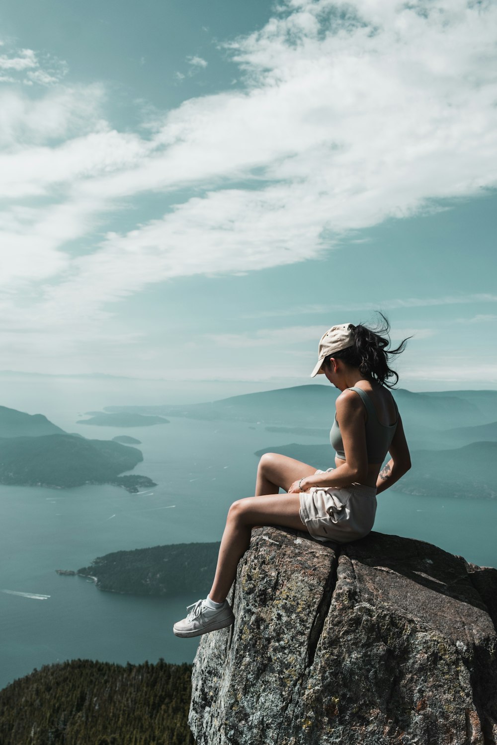 woman in black bikini sitting on rock near body of water during daytime