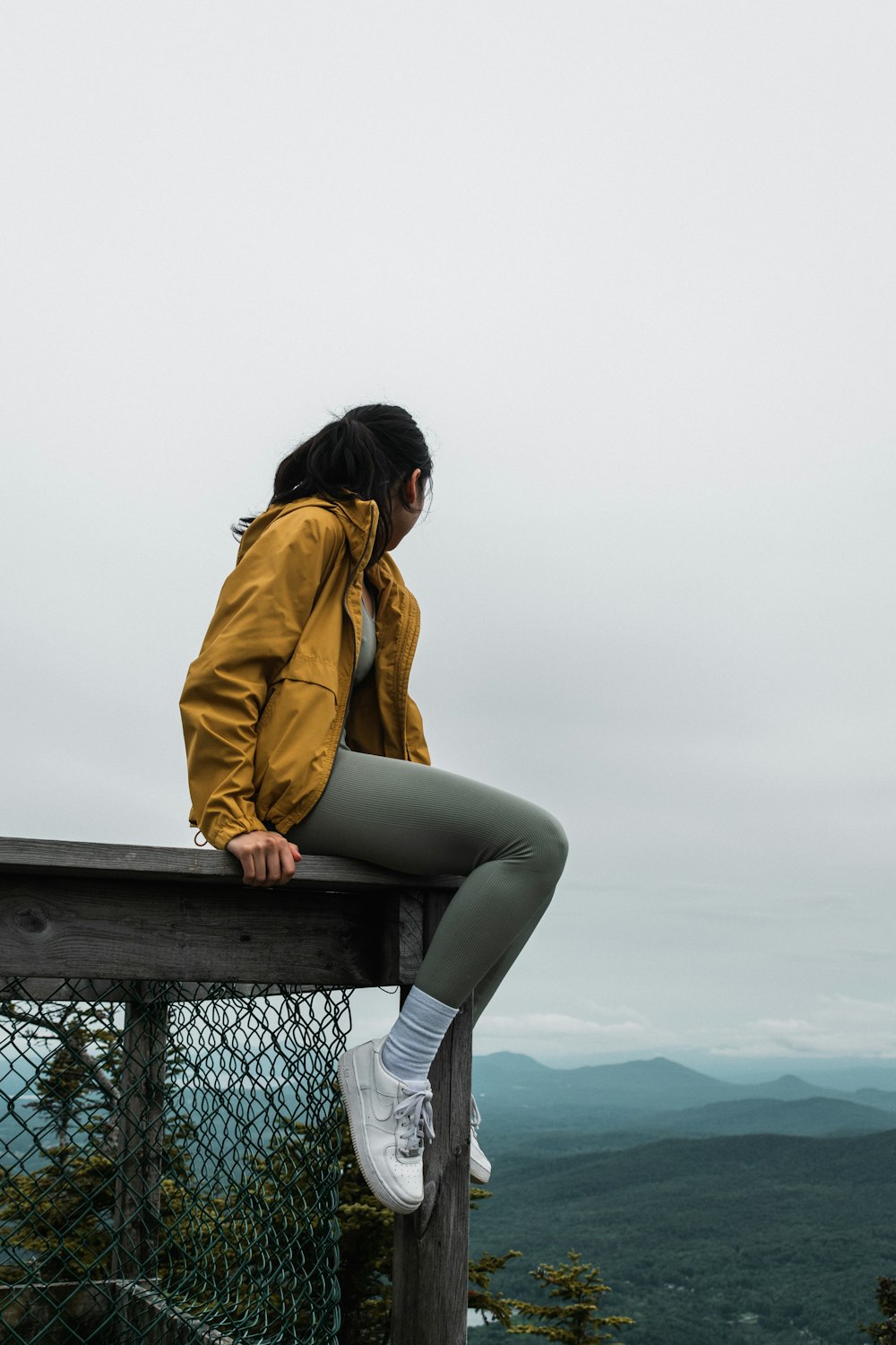 woman in brown jacket and gray pants sitting on brown wooden bench