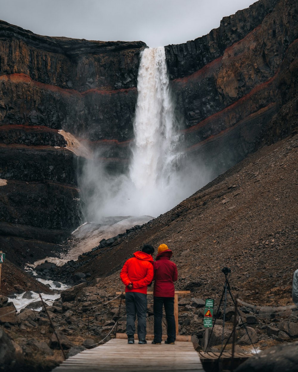 man in red jacket standing near waterfalls during daytime