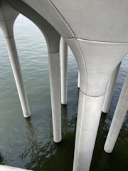 Several sturdy concrete pillars extending vertically into a body of water, providing structural support from above the surface. The water reflects the light, showing subtle ripples, and the architecture is marked by smooth, clean lines.