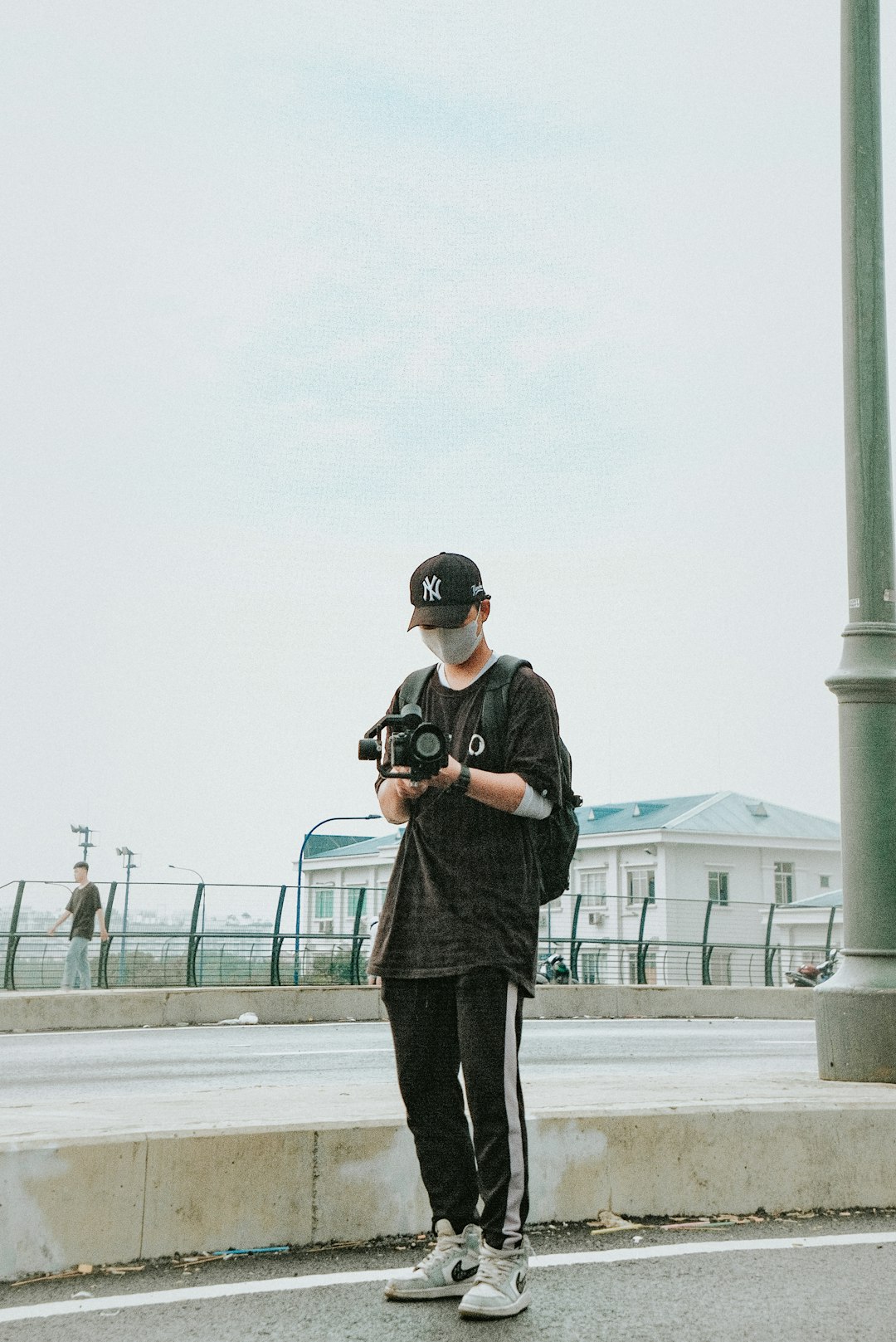 man in black jacket and black pants holding black dslr camera standing on gray concrete floor