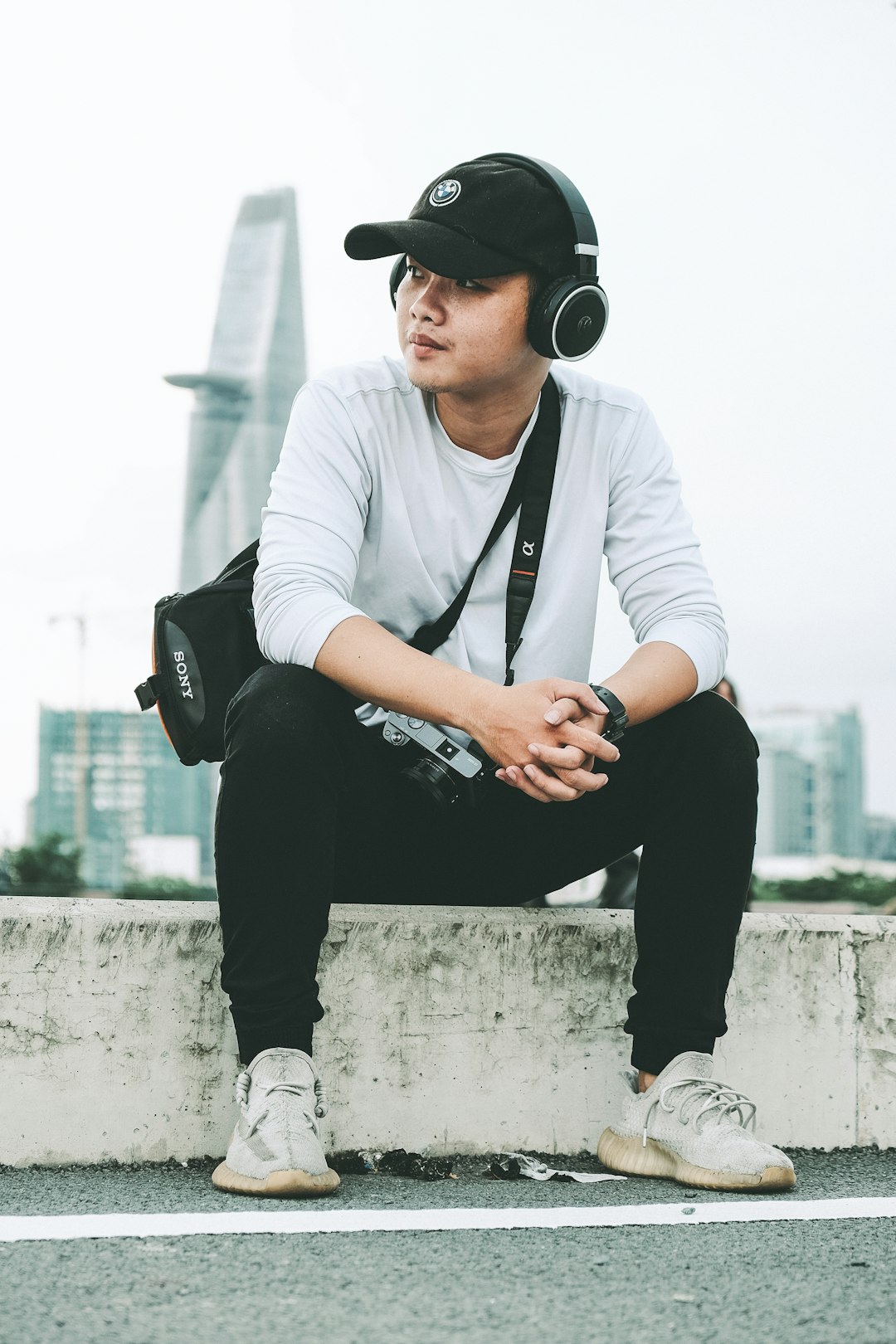 man in white dress shirt and black pants wearing black cap sitting on concrete wall during