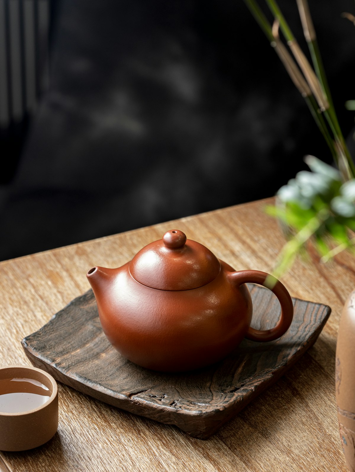 Ceramic teapot pouring hot water over loose-leaf tea in a glass cup