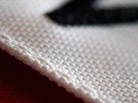 A close-up view of a textured fabric material, showcasing the intricate weave of the threads. The white cloth appears to be craft or industrial-grade with a clear focus on its structure, highlighting each individual fiber and strand.