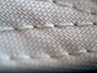 A close-up view of a textured fabric surface, showing intricate stitching and woven threads. The fabric appears to be tightly knit, with visible threads that form a repetitive pattern.