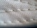 A close-up view of a textured fabric surface, showing intricate stitching and woven threads. The fabric appears to be tightly knit, with visible threads that form a repetitive pattern.