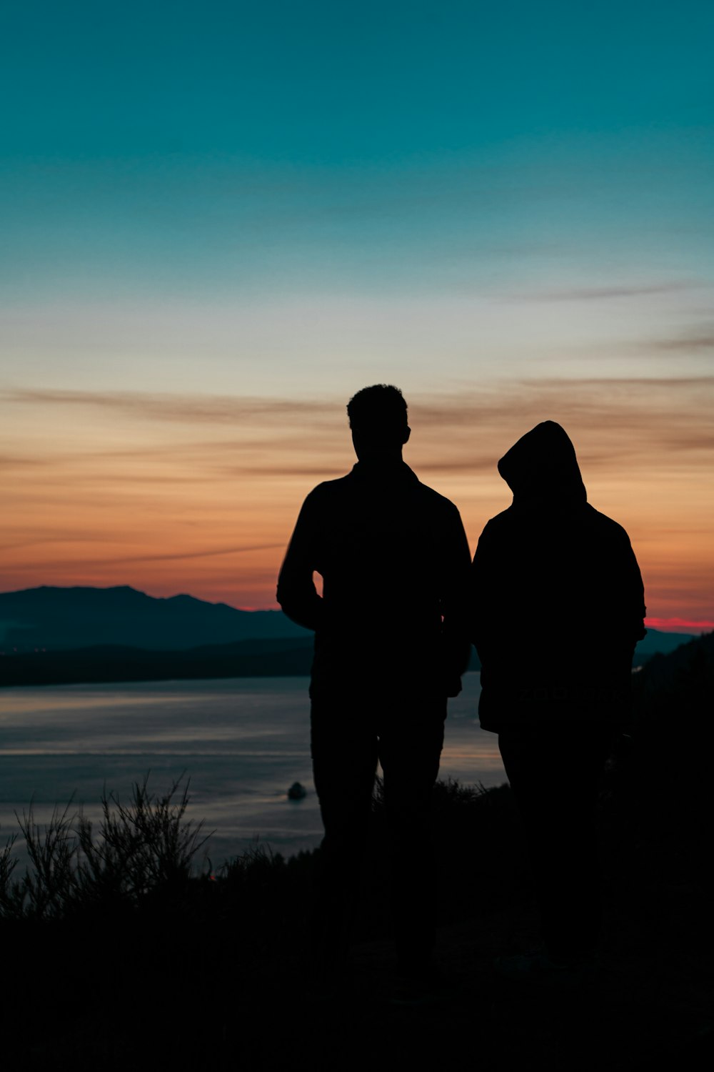 silhouette of man and woman standing near body of water during sunset