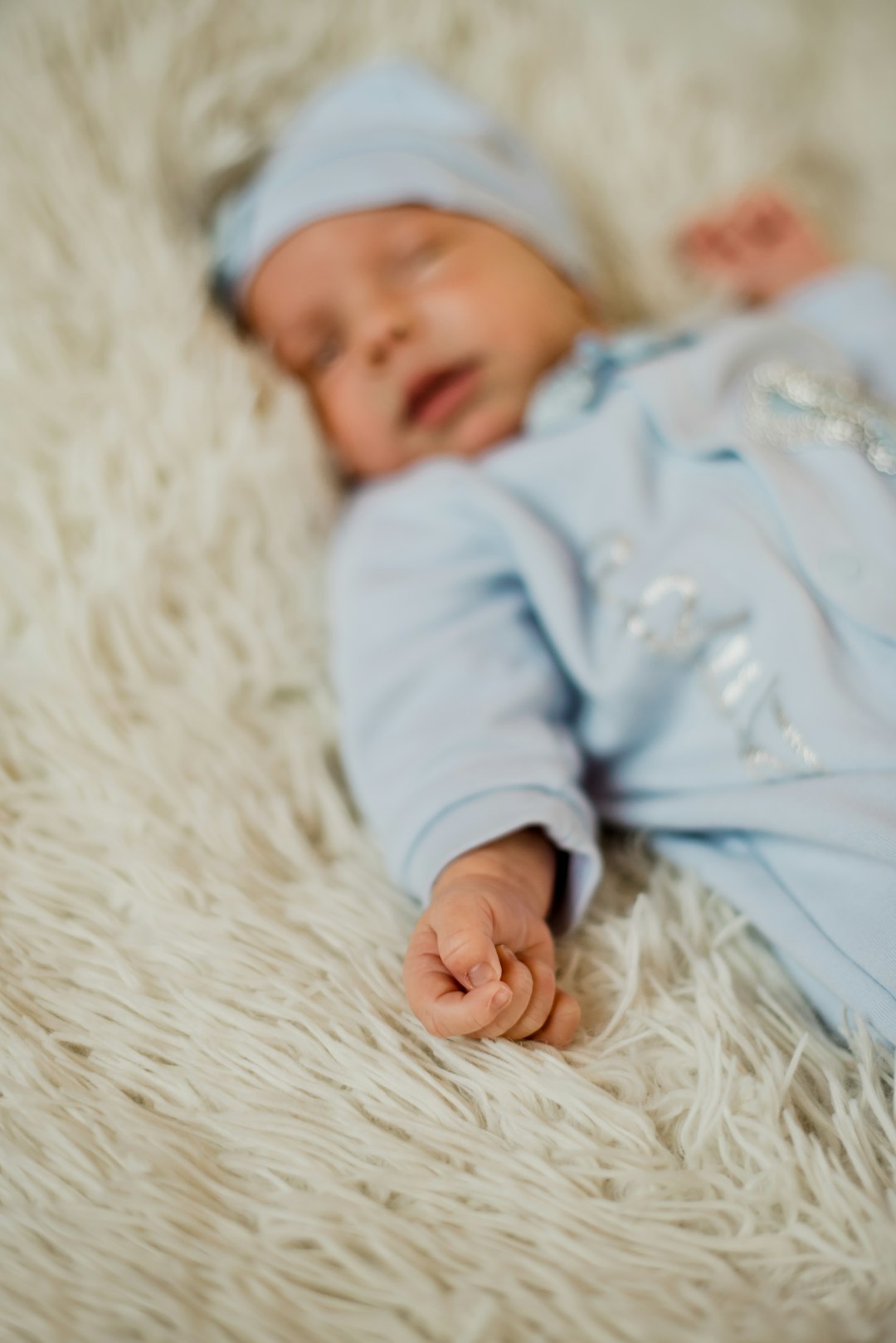 baby in blue onesie lying on white textile