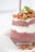 A layered glass dessert featuring chia seed pudding and yogurt, topped with granola, berries, and a few sprigs of fresh greenery. The dessert sits on a white background, creating a clean and bright presentation.