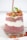 A glass filled with layered chia pudding made from chia seeds and yogurt, topped with granola, sliced strawberries, and a sprig of fresh greens. The chia pudding has a pinkish hue due to the mixture with berry juice, giving it a colorful and appealing appearance.