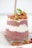 A glass filled with layered chia pudding made from chia seeds and yogurt, topped with granola, sliced strawberries, and a sprig of fresh greens. The chia pudding has a pinkish hue due to the mixture with berry juice, giving it a colorful and appealing appearance.