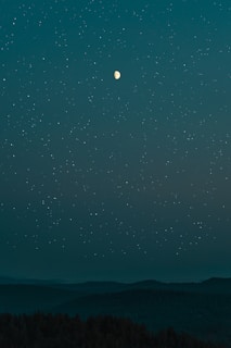 A serene night sky filled with stars and a glowing full moon over a tranquil landscape.
