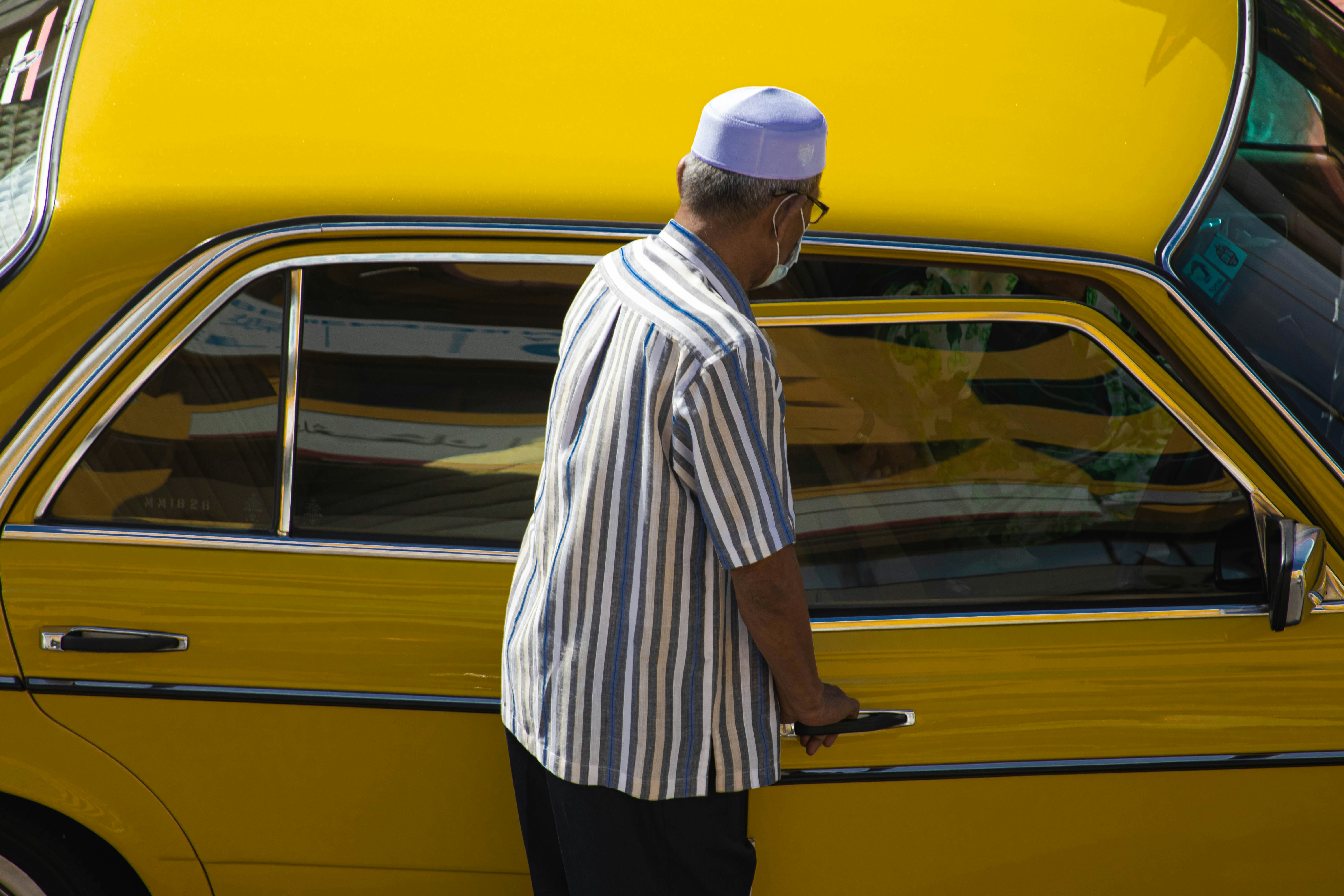 man in white and brown stripe dress shirt and black pants standing beside yellow car