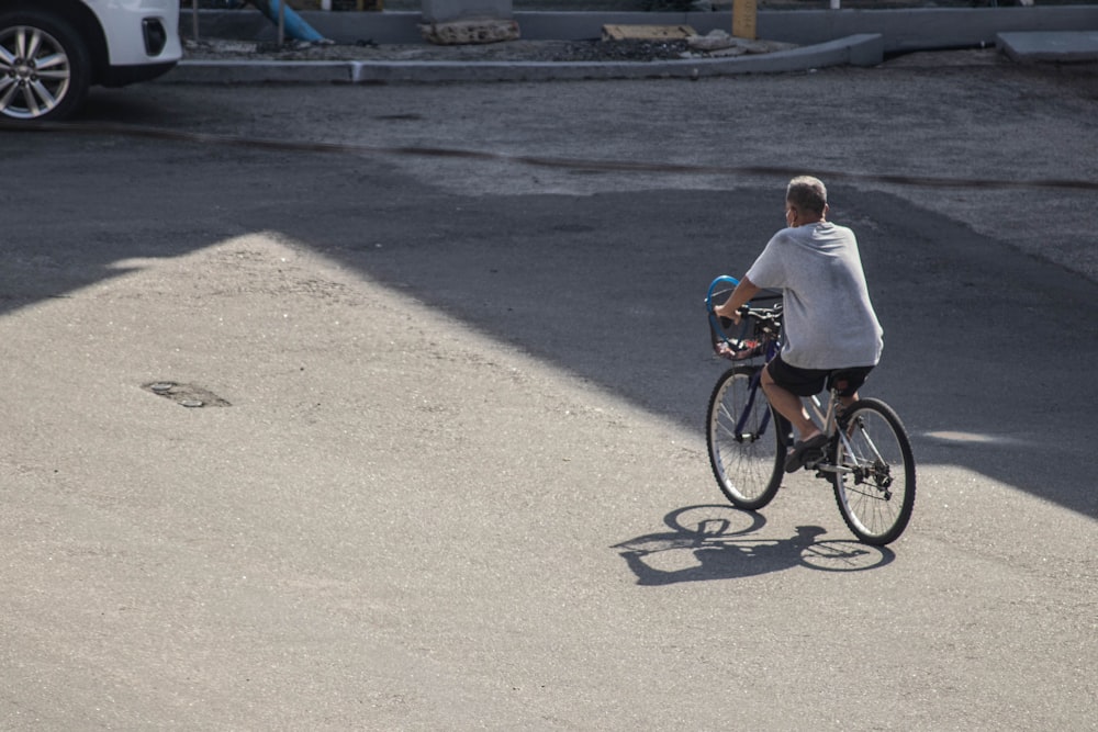 man in white shirt riding bicycle on gray concrete road during daytime