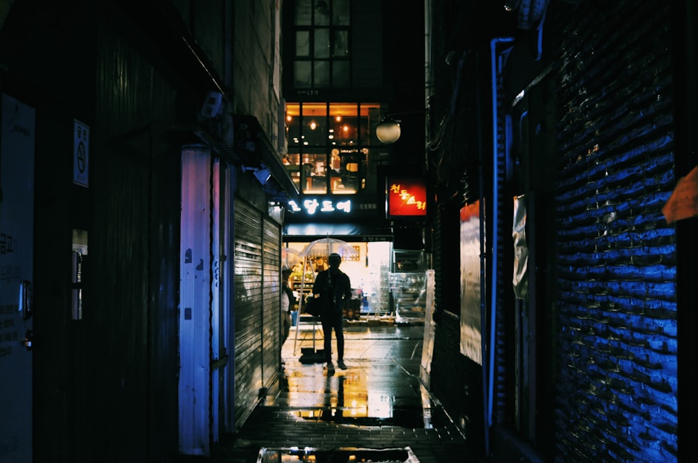 man in black jacket walking on sidewalk during night time