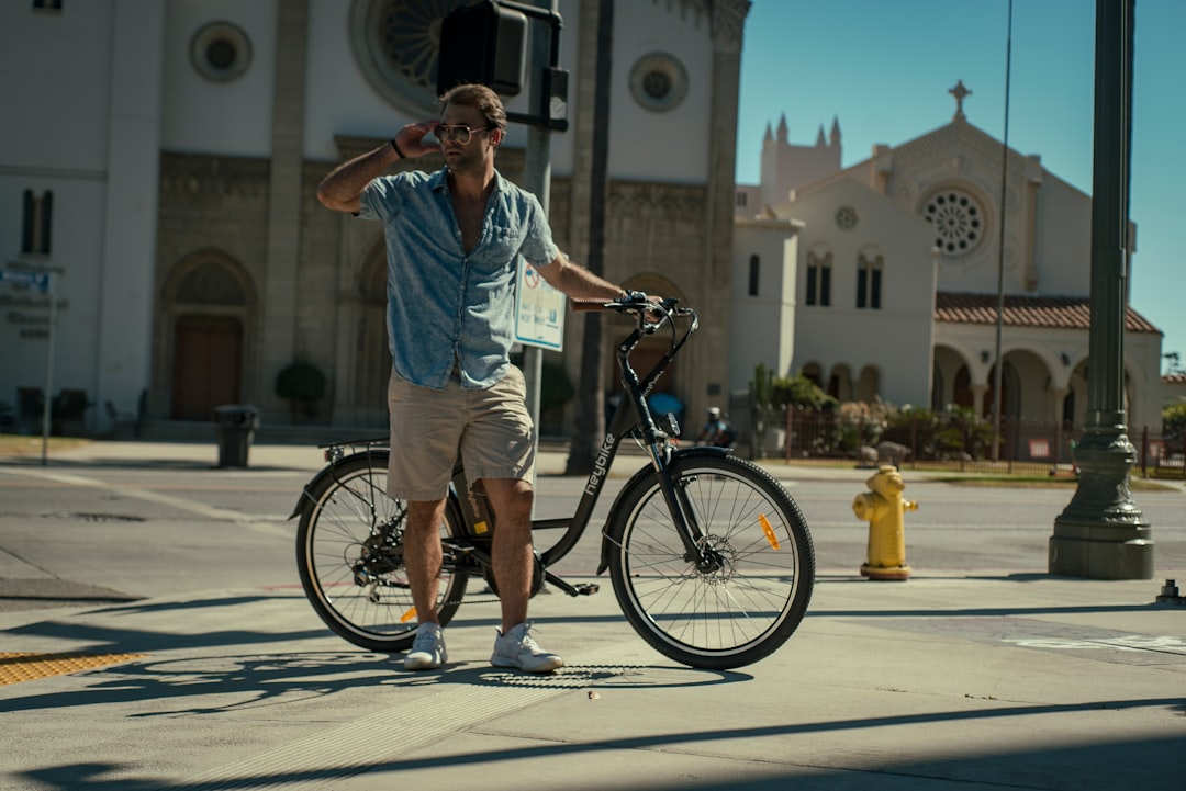 man in blue dress shirt and brown shorts standing beside black bicycle during daytime