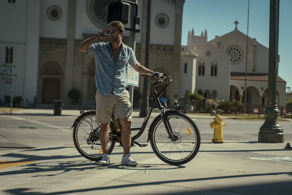 man in blue dress shirt and brown shorts standing beside black bicycle during daytime