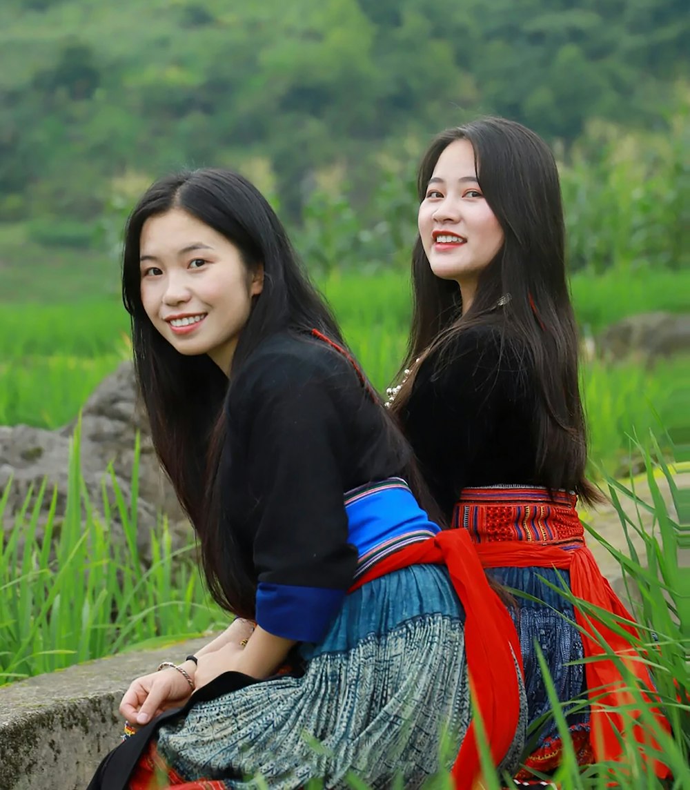 2 women sitting on brown wooden fence during daytime