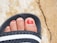 Close-up of a happy woman showing her freshly pedicured feet with bright nail polish.