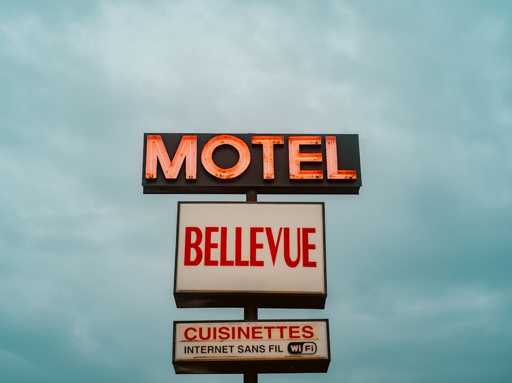a motel sign and a restaurant sign against a cloudy sky