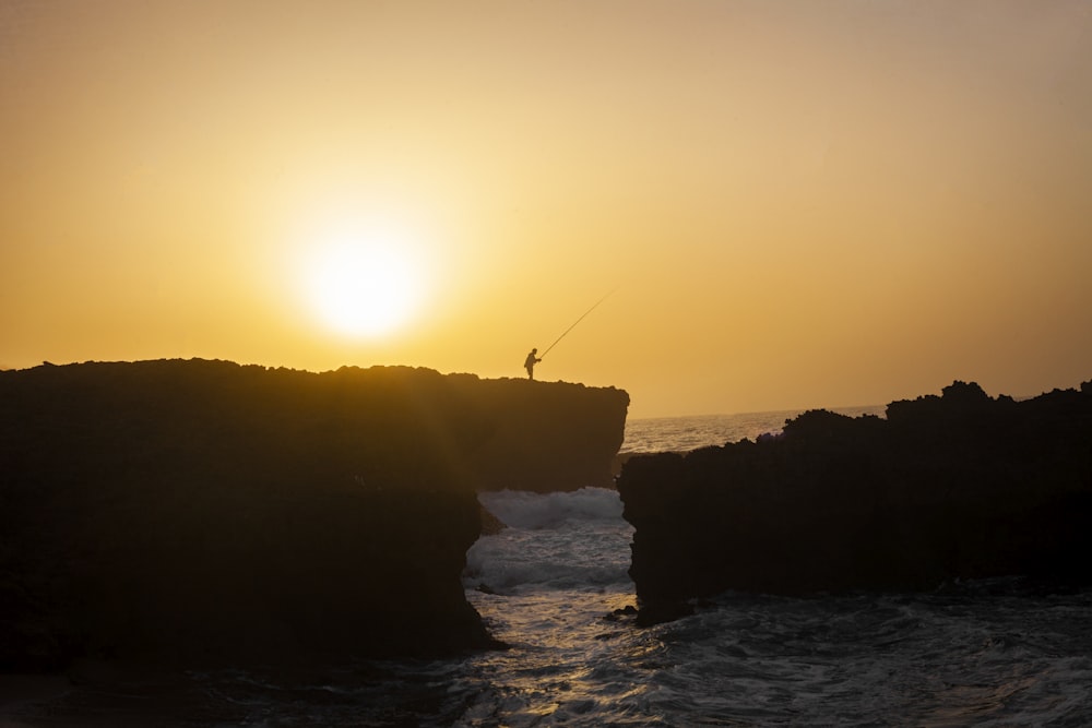 silhouette of a person fishing on sea during sunset