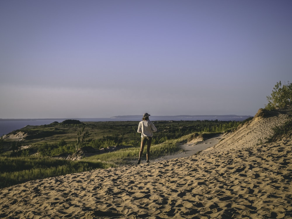 woman in white shirt and black pants walking on brown sand during daytime