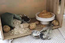 A warm, inviting kitchen scene featuring jars of ghee, bottles of oil, and sacks of flour on a rustic wooden counter.