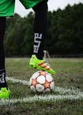 person in green and black soccer jersey kicking soccer ball on green grass field during daytime