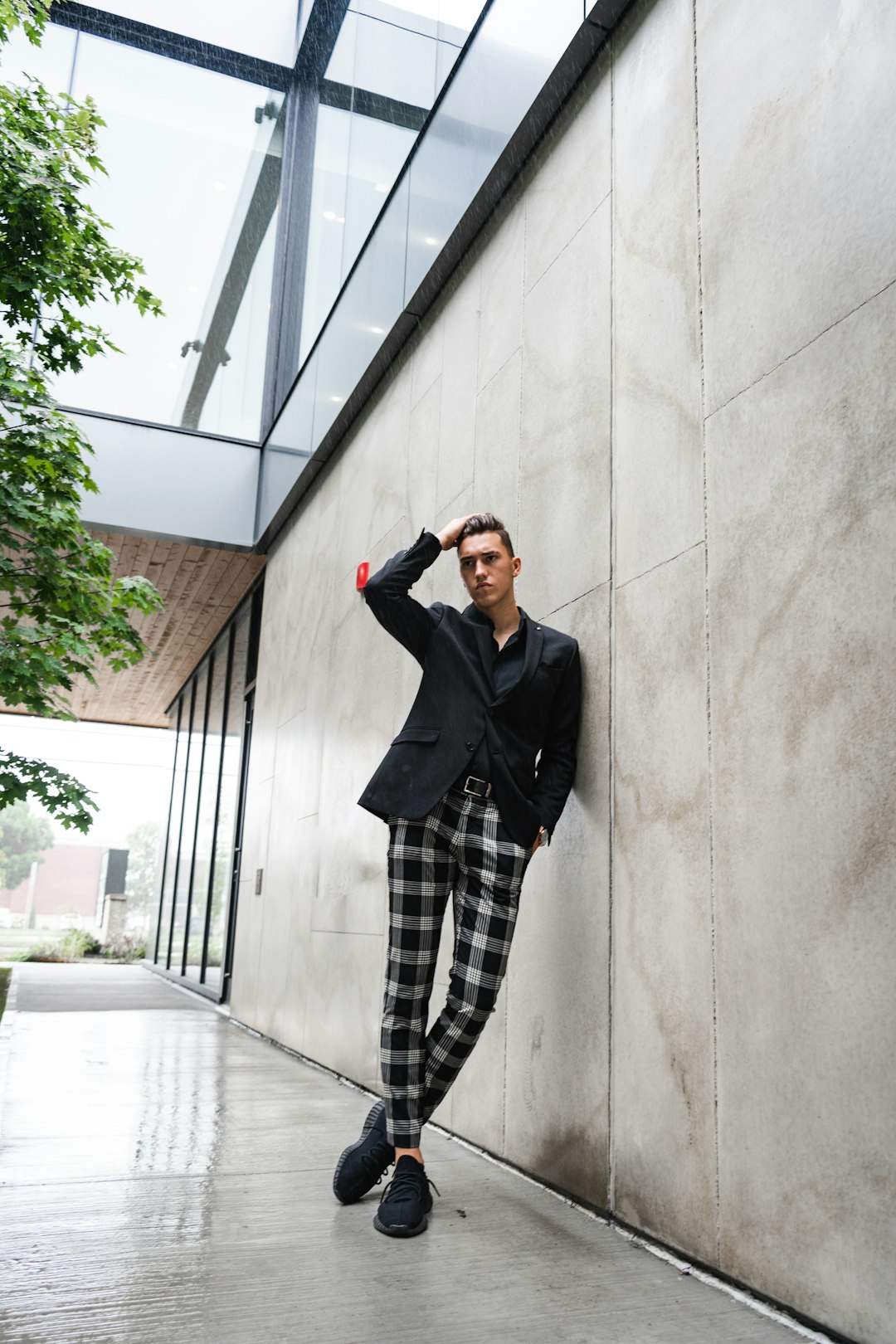 man in black blazer and gray and white plaid pants standing beside white concrete wall