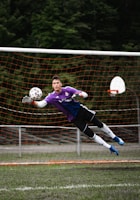 A goalkeeper diving mid-air to save a powerful shot during an intense match.
