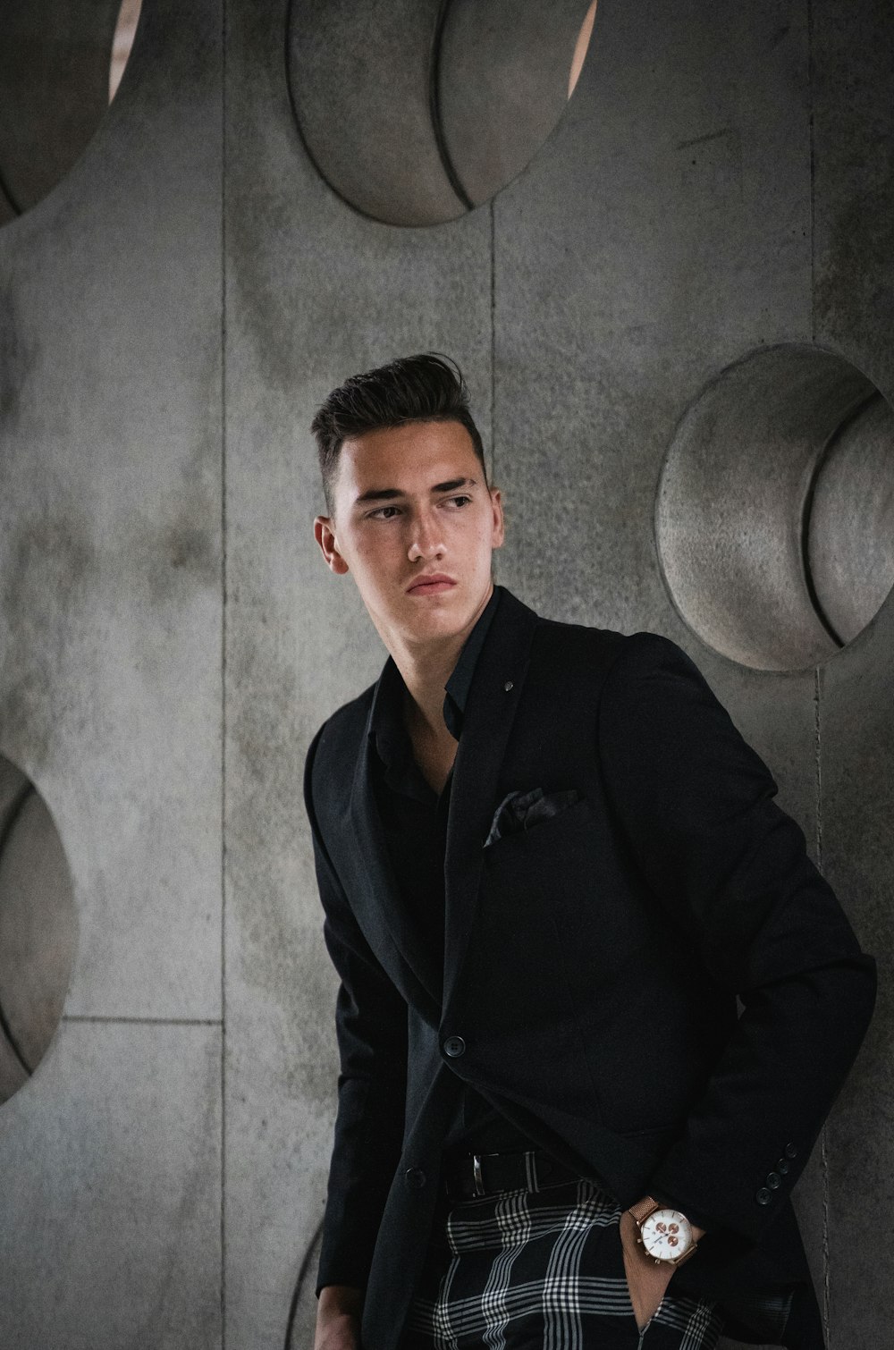 man in black button up jacket standing beside gray wall