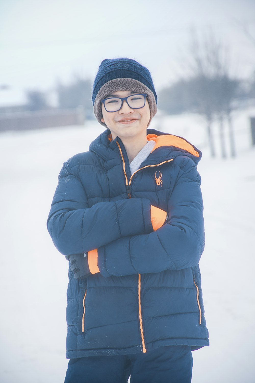 lächelnde Frau in blauer Jacke und schwarzer Strickmütze, die tagsüber auf schneebedecktem Boden steht