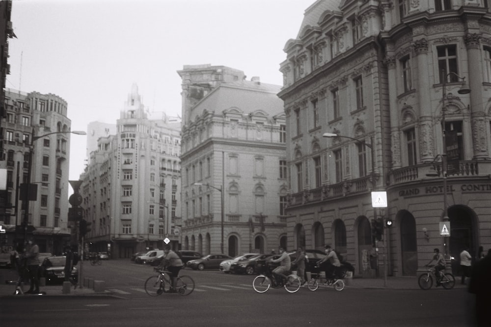 grayscale photo of people riding motorcycle near building