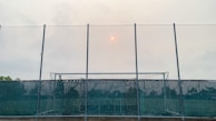 View of a sports field surrounded by strong metal mesh fencing under bright daylight.