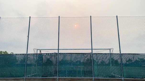 Wide shot of a sports field enclosed by sturdy metal mesh fencing under a clear sky.