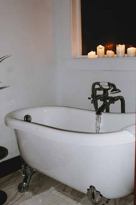 A cozy clawfoot tub surrounded by flickering candles and delicate hanging plants