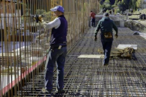 Construction workers unloading TMT steel bars at a busy building site.