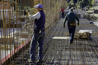 Construction workers unloading TMT steel bars at a busy building site.