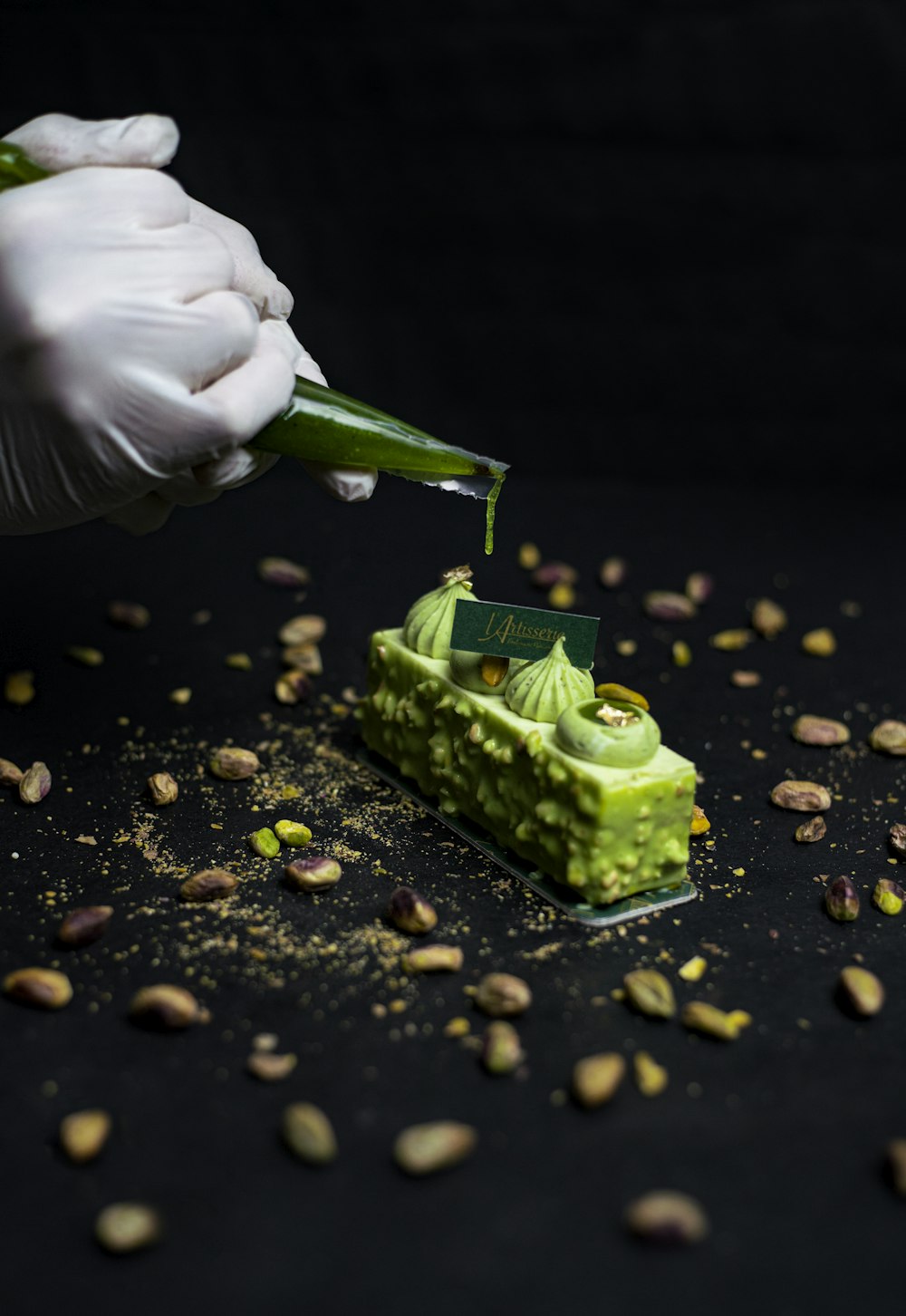 a person in white gloves is putting a green substance on a piece of cake