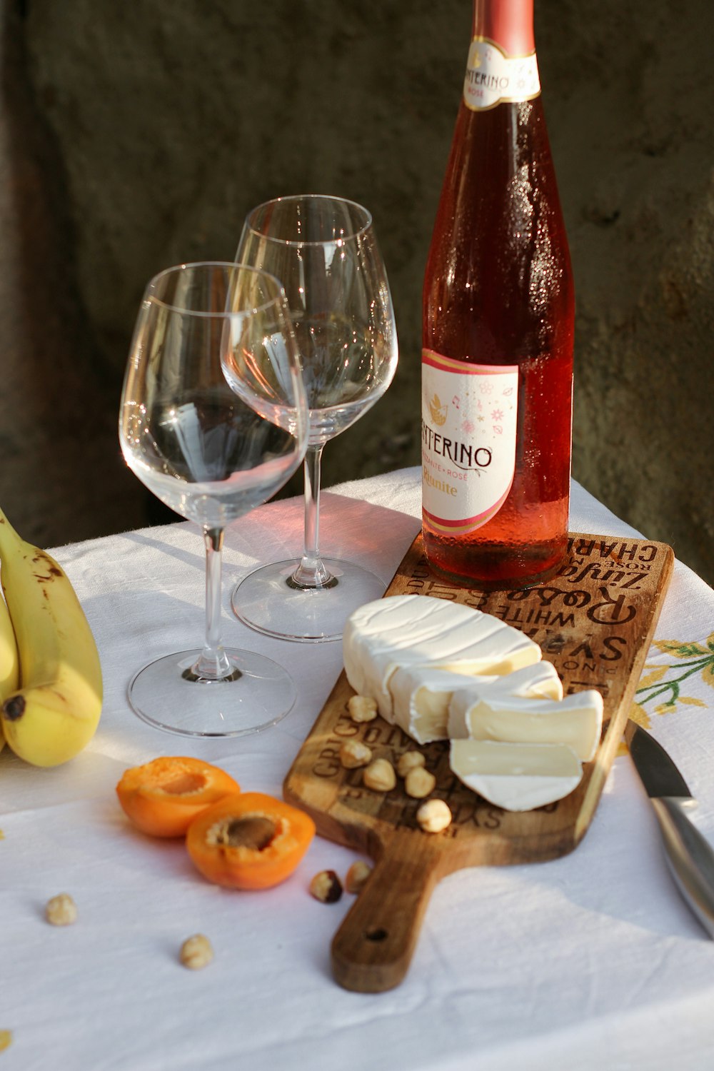 taça de vinho transparente ao lado de tábua de cortar madeira marrom com banana fatiada e pão integral