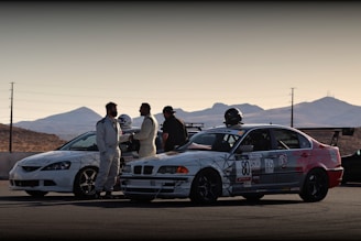 group of people standing beside white and black coupe on road during daytime