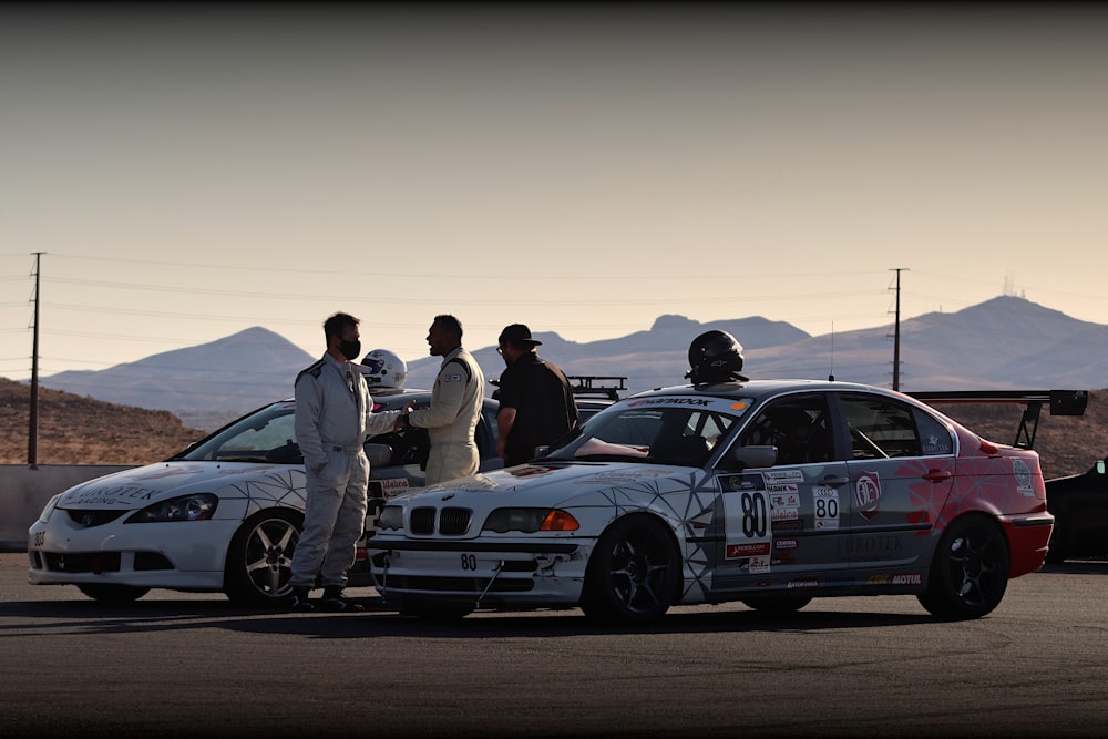 group of people standing beside white and black coupe on road during daytime