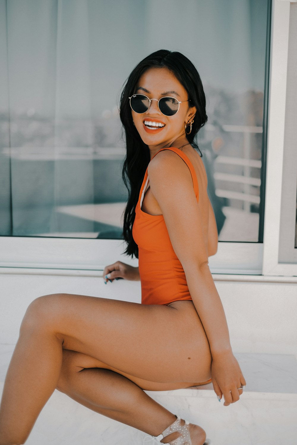 woman in orange tank top wearing black sunglasses sitting on white table