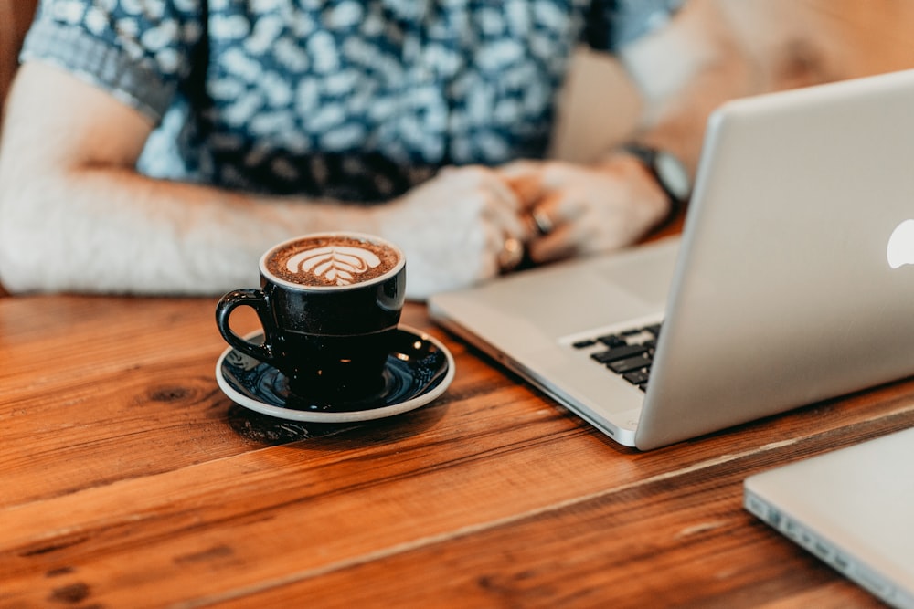 black ceramic mug on black saucer beside macbook pro