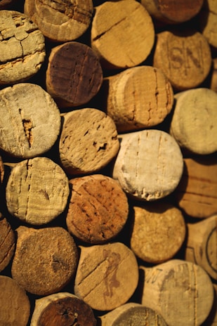 A collection of wine corks tightly arranged together. The corks vary in texture and shade, displaying a range of natural browns and beiges. Each cork shows unique wear patterns and markings from bottle openings.